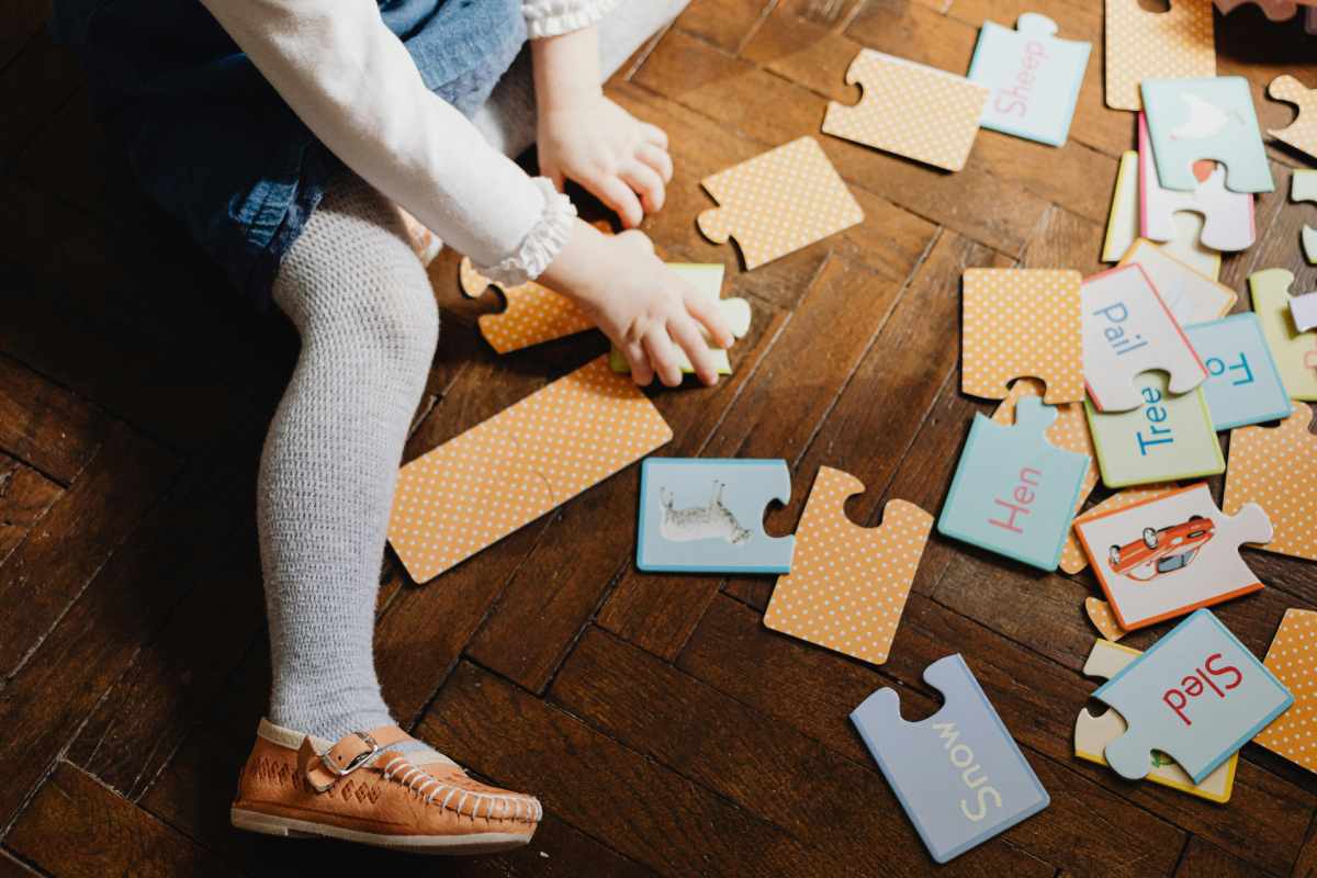 Una bambina seduta sul parquet che gioca con un puzzle